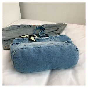 Détail du sac cabas en denim bleu avec bords effilochés et nœud décoratif en soie