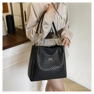 Detail of black woven tote bag featuring gold chain strap and textured leather finish