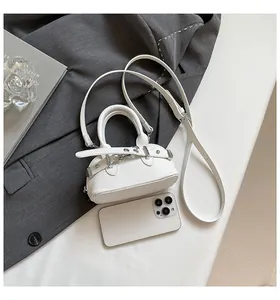 Mini sac bandoulière blanc à motif litchi avec boucles moto à côté d'un téléphone