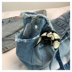 Détail d'un grand cabas en denim bleu clair délavé avec bords effilochés et foulard
