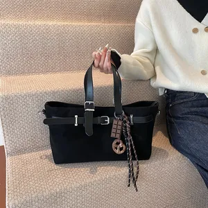 Black matte leather tote bag with decorative buckles and charms shown in a lifestyle setting