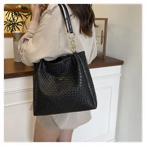 Detail of black woven tote bag featuring gold brand plate and metallic chain shoulder strap