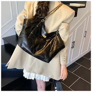 Detail of a black quilted tote bag with gold chain strap shown on a model