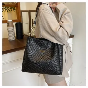 Detail of black woven leather tote bag with gold logo plate and chain strap on shoulder