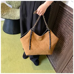 Detail of quilted tote bag with golden twist lock and chain strap on a green rug