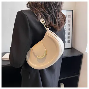 Detail of a beige crescent shoulder bag with gold metal U-buckle worn on a black blazer