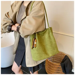 Detail view of avocado green suede tote bag with decorative wooden bead charm accessory