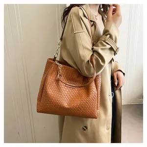 Brown woven tote bag with gold metal logo worn with beige trench coat for a city look