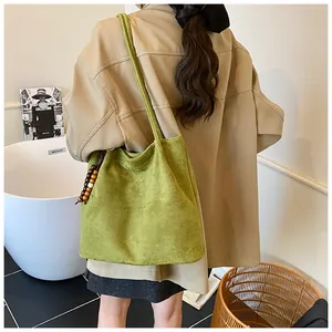 Close-up of green suede tote bag with decorative wood beads and long shoulder strap