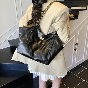Large black quilted tote bag with gold chain strap shown on model's shoulder