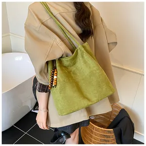 Close-up of retro green suede tote bag with wooden bead charm and long shoulder strap