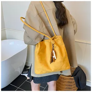 Detail of yellow suede tote bag with wooden bead tassel shown on model in studio