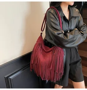 Close-up of deep wine red suede shoulder bag with dense fringe details and wide strap