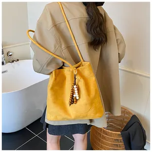 Close-up of yellow suede shoulder bag featuring a vintage wooden beaded tassel pendant