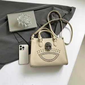 Beige tote bag with silver skull and studs detail on a grey suit background