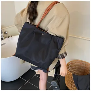 Detail van een grote zwarte shopper met bruine leren handvatten en gladde waterdichte stof
