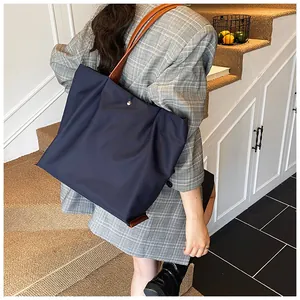 Detail van de marineblauwe tote bag met bruine leren riemen en metalen knoop op model