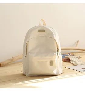 Detail of minimalist beige oxford cloth backpack showing leather logo and zipper pocket texture