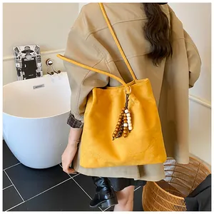 Detail of yellow suede tote bag featuring wooden bead tassels and fringe decoration