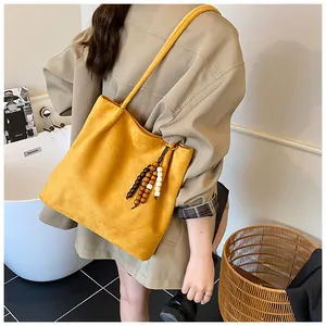 Detail of yellow faux suede tote bag featuring a decorative wooden bead tassel pendant