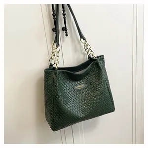 Detail of dark green woven tote with golden logo plaque and chain leather strap