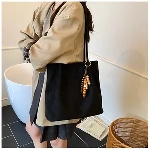 Suede tote bag in black featuring a wooden bead charm and long shoulder straps