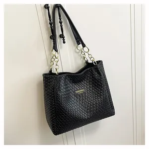 Close-up of black woven texture tote bag featuring gold chain straps and metal logo plate