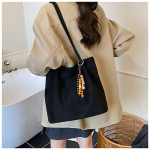 Detail view of black faux suede tote bag with colorful wooden bead charm and slim shoulder strap