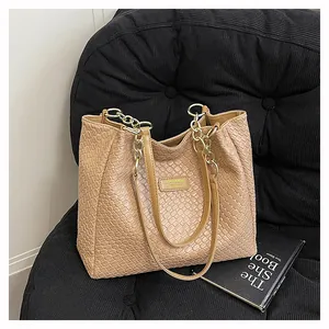 Detail view of woven texture tote bag with golden metal logo and chain strap