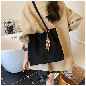 Detail of black suede tote bag with vintage wooden bead charm and slim leather straps