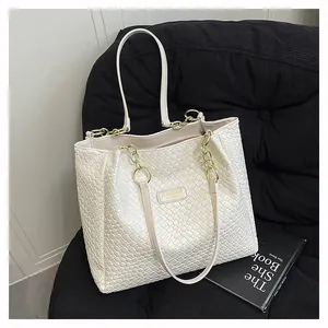 Detail view of cream white woven tote bag with metallic logo plate and gold chain strap