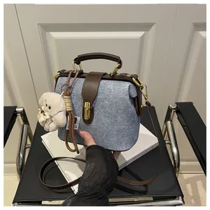 Detail view of denim doctor bag with brown leather handles, gold buckle, and plush charm