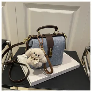 Detail of blue denim doctor bag with brown leather trim and a white plush puppy charm