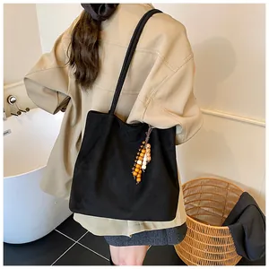 Detail of large black suede tote bag with colorful bead charm on shoulder of a model