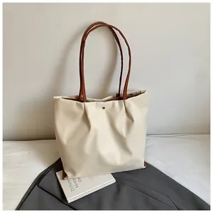 Detail van minimalistische geplooide shopper met bruine hengsels en zilveren drukknoop
