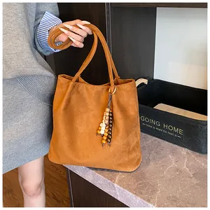 Close-up of brown suede tote bag featuring a decorative wooden bead and leather tassel charm