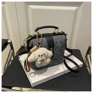 Detail of tweed doctor bag featuring gold metal clasp and a plush dog charm on strap