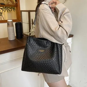 Black woven tote bag with gold chain and metal logo plate shown in casual cafe setting