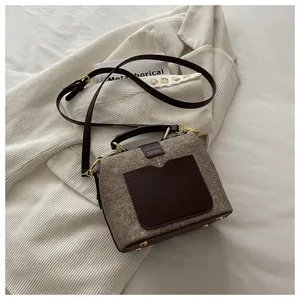 Detail view of the brown tweed bag base with golden protective studs and leather handle