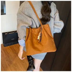 Detail of retro brown suede tote bag featuring a decorative wooden beaded tassel pendant