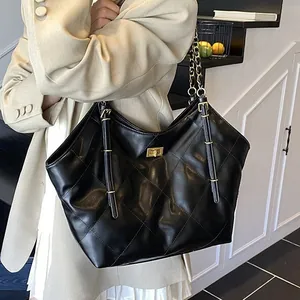 Black quilted tote bag with golden lock and chain strap carried by a fashion model