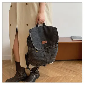 Detail of dark grey denim backpack with a leather patch being held by a person