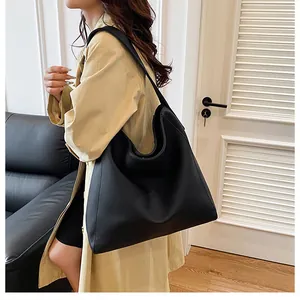 Detalle del bolso tote grande de cuero sintético negro llevado al hombro con un abrigo beige