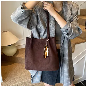 Detail of a dark brown suede tote bag featuring a decorative wooden bead tassel charm