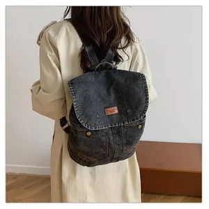 Detailed back view of a large washed denim backpack with metal buckles on grey straps