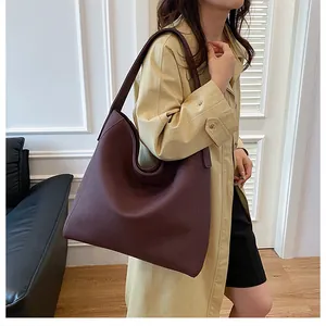 Primer plano de un gran bolso tote de cuero rojo oscuro usado con una gabardina color beige