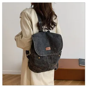 Detail of dark grey vintage denim backpack featuring leather logo patch and top handle