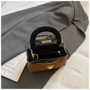 Quilted brown chain bag with black top handle and gold hardware on grey suit jacket
