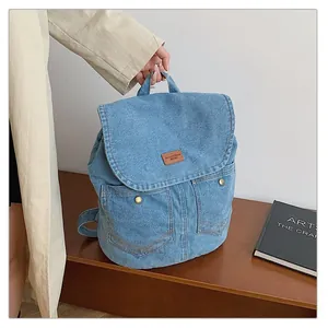 Detail of blue denim backpack with brown leather logo patch and metal snap buttons