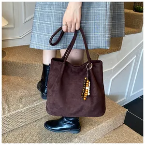 Detail of dark brown suede tote bag featuring a vintage wooden bead charm accessory